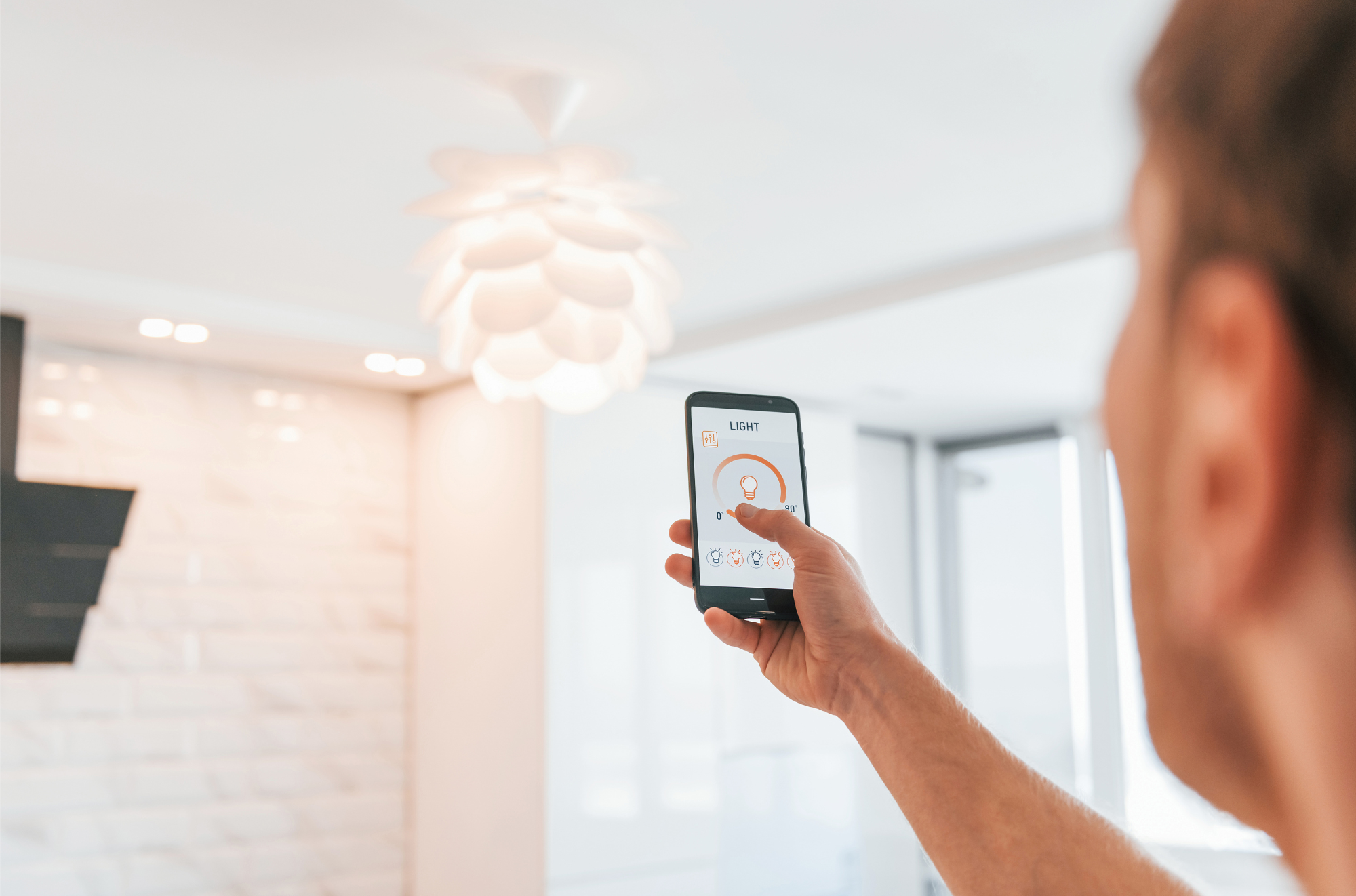 Ein Mann steuert über die Visualisierung auf seinem Smartphone eine Lampe an der Decke.